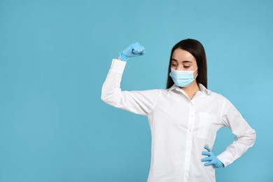 Photo of Woman with protective mask and gloves showing muscles on light blue background, space for text. Strong immunity concept