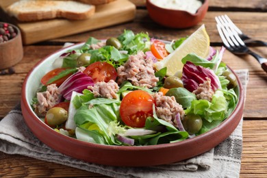 Photo of Plate of delicious salad with canned tuna and vegetables served on wooden table