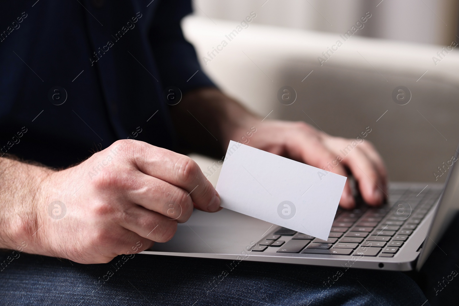 Photo of Man with laptop holding blank business card on blurred background, closeup