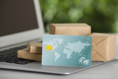 Online payment concept. Bank card and small boxes with laptop on white table, closeup