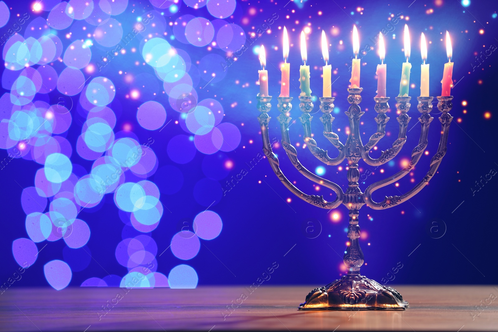 Image of Hanukkah celebration. Menorah with burning candles on wooden table against blue background with blurred lights, space for text