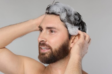 Photo of Handsome man washing his hair with shampoo on grey background, closeup
