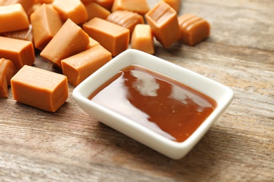 Photo of Delicious caramel candies and sauce on wooden background