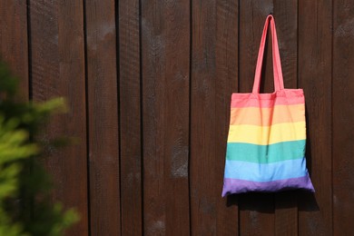 Photo of Rainbow bag hanging on wooden background, space for text. LGBT pride