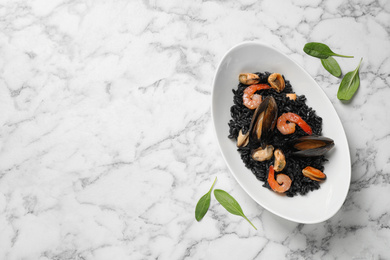 Delicious black risotto with seafood on white marble table, flat lay. Space for text