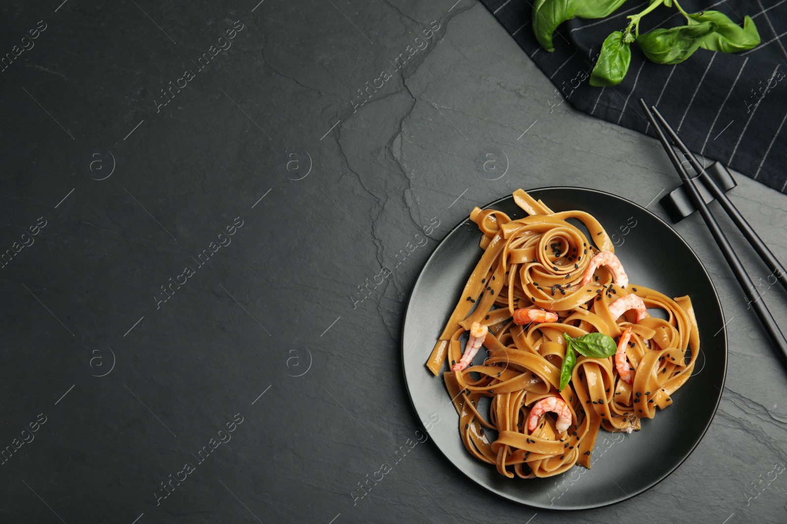 Photo of Tasty buckwheat noodles with shrimps served on black table, flat lay. Space for text