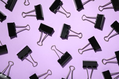 Photo of Black binder clips on violet background, flat lay. Stationery items