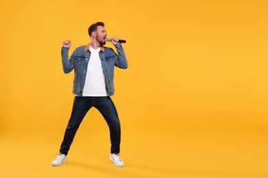 Photo of Handsome man with microphone singing on yellow background. Space for text
