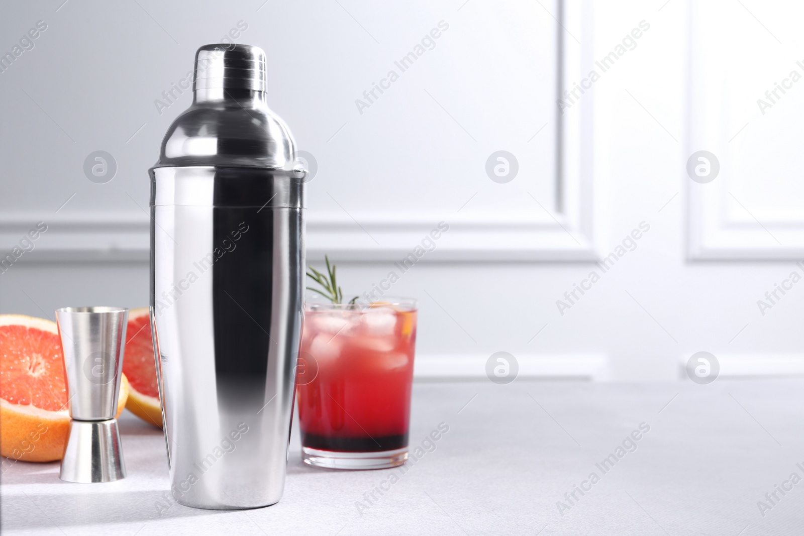 Photo of Metal shaker, delicious cocktail, jigger and grapefruit on light grey table, space for text