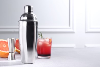 Photo of Metal shaker, delicious cocktail, jigger and grapefruit on light grey table, space for text