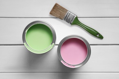 Cans of pink and green paints with brush on white wooden table, flat lay