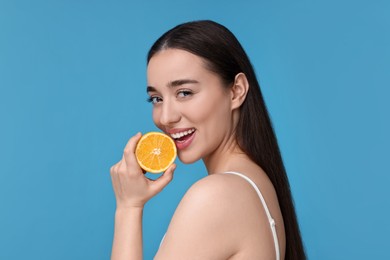 Photo of Beautiful young woman with piece of orange on light blue background