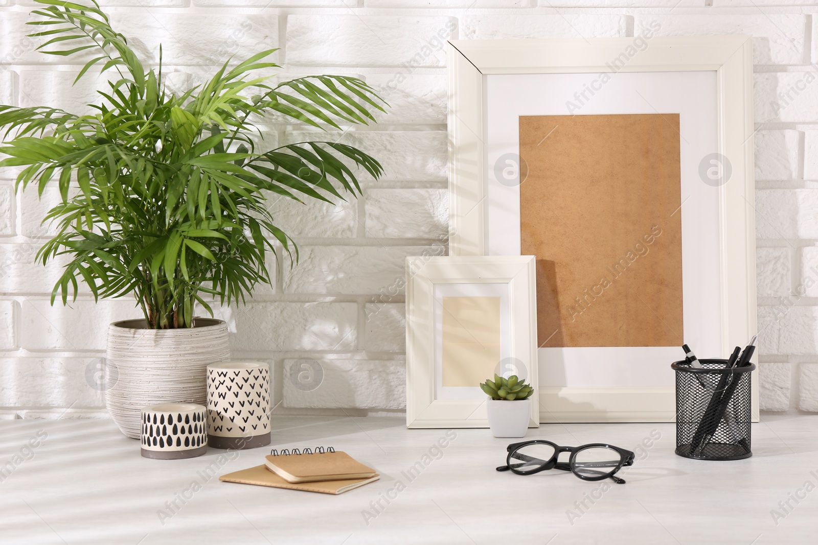 Photo of Stylish office workplace. Decor elements, glasses and stationery on white table near brick wall