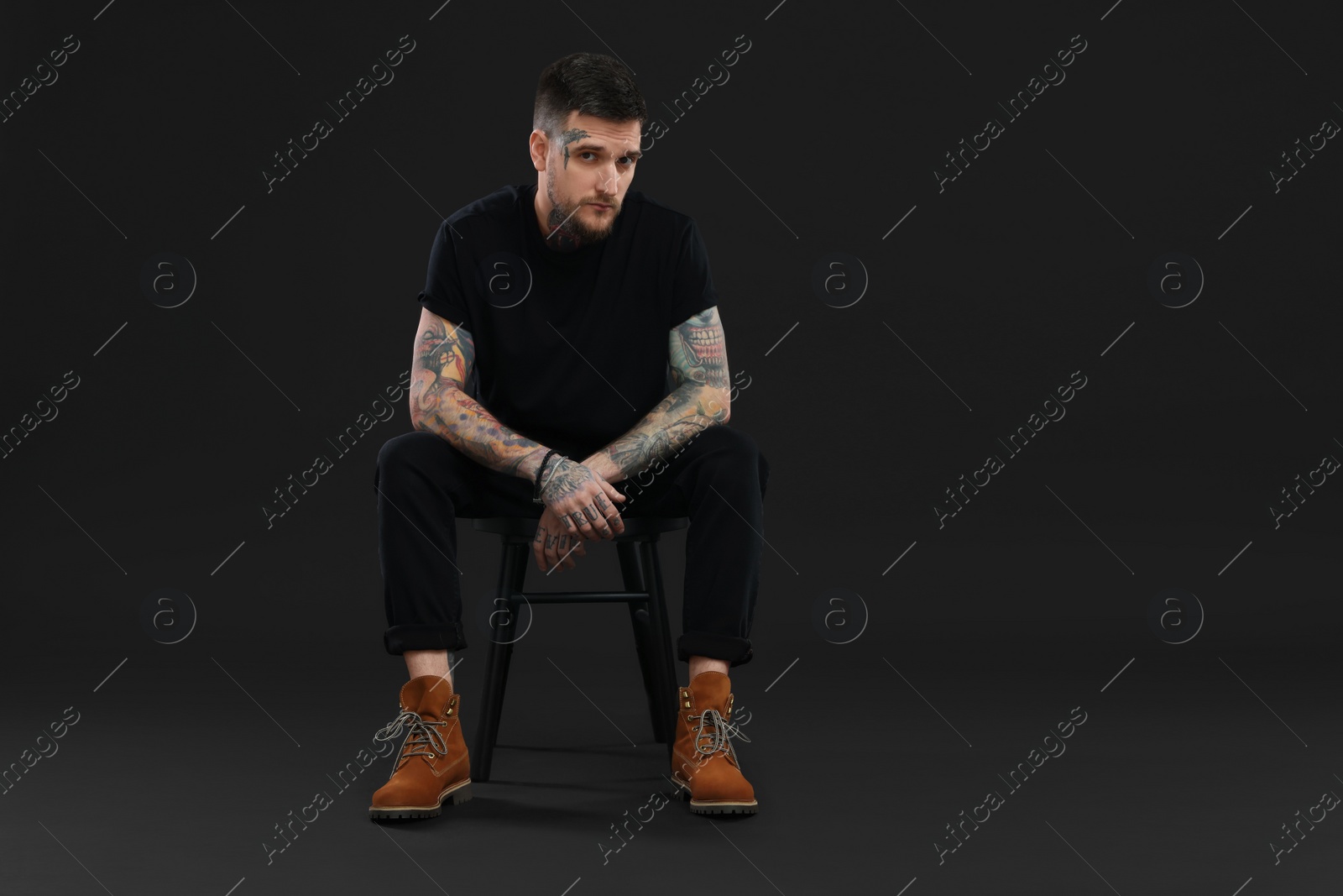 Photo of Portrait of handsome hipster man sitting on chair against black background. Space for text