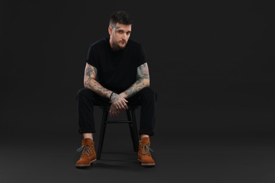 Photo of Portraithandsome hipster man sitting on chair against black background. Space for text