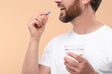Photo of Man with glass of water taking pill on beige background, closeup