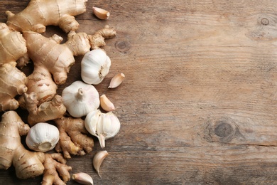 Photo of Ginger and fresh garlic on wooden table, flat lay with space for text. Natural cold remedies
