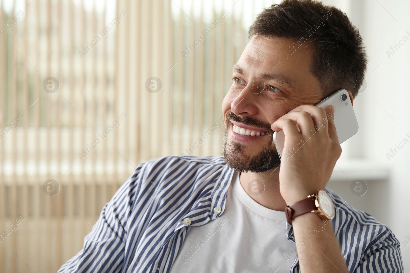 Photo of Happy handsome man talking on smartphone indoors