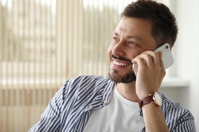Photo of Happy handsome man talking on smartphone indoors