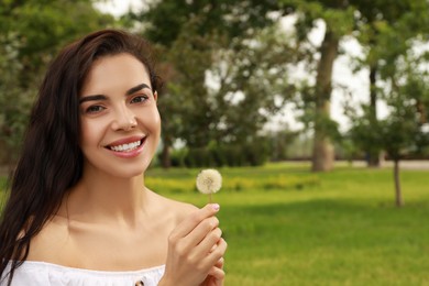 Photo of Beautiful young woman with dandelion in park, space for text. Allergy free concept