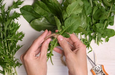 Photo of Woman tying bunchfresh green leaves with twine at white wooden table, top view
