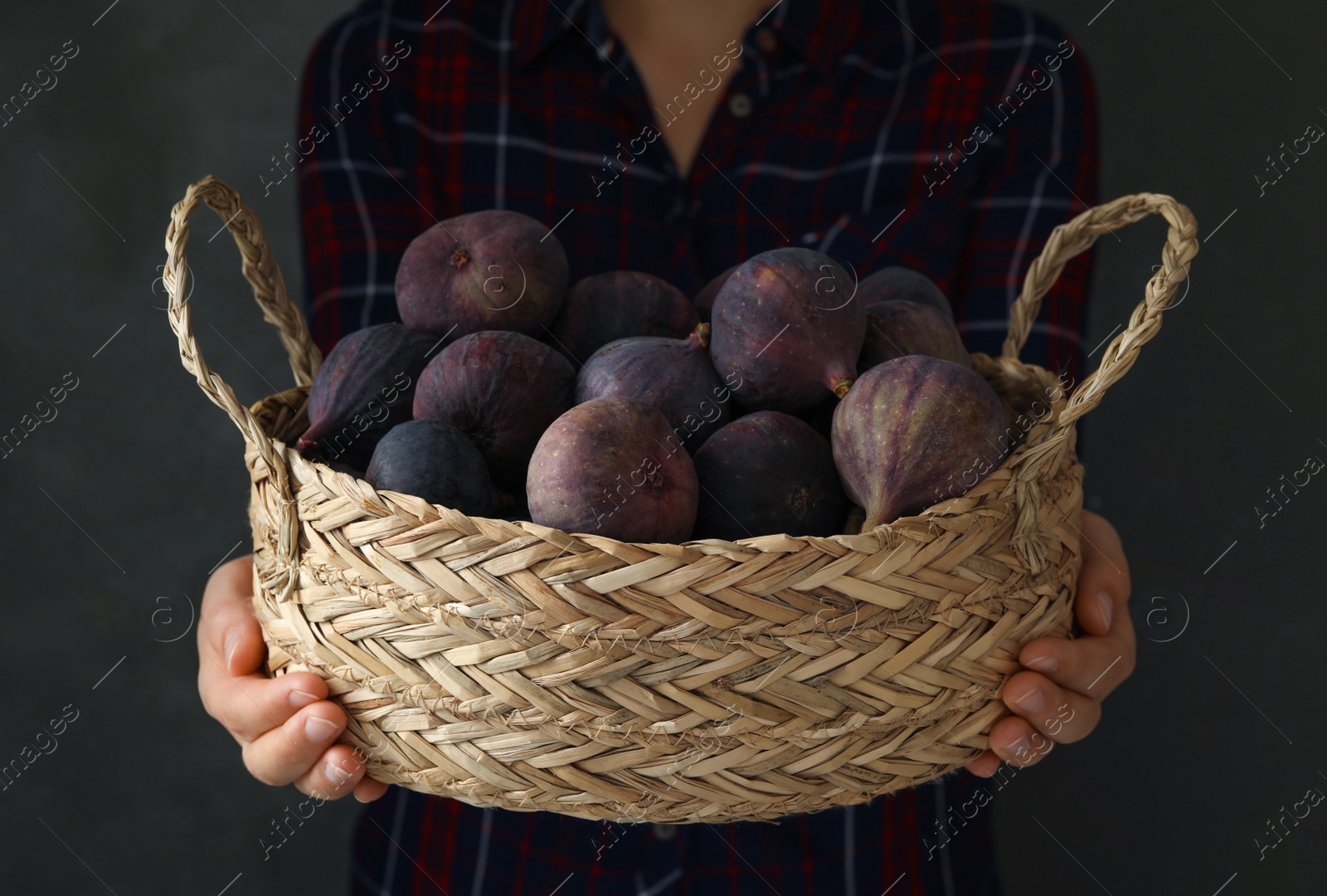 Photo of Woman holding basket with tasty raw figs on grey background, closeup