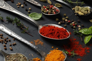 Different herbs and spices with spoons on black table, closeup