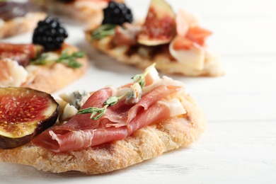 Photo of Sandwich with ripe figs and prosciutto served on white wooden table, closeup