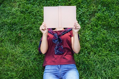 Woman reading book while lying on green grass outdoors, top view