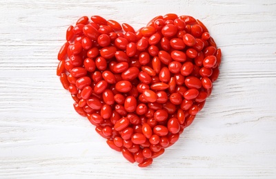 Photo of Heart shaped pile of fresh ripe goji berries on white wooden table, top view