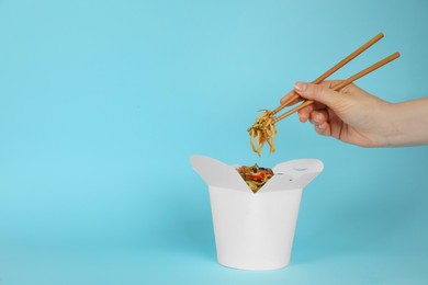 Photo of Woman eating wok noodles with chopsticks from box on light blue background, closeup. Space for text