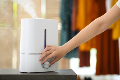 Photo of Woman turning on air humidifier indoors, closeup