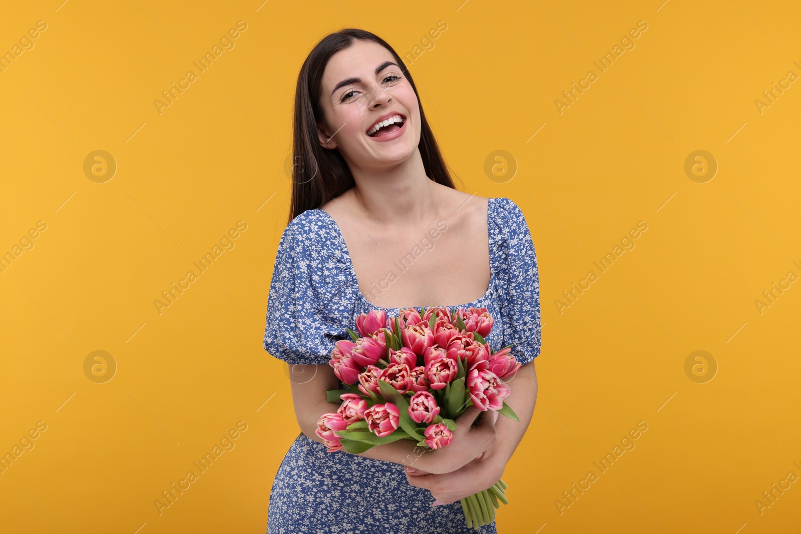 Photo of Happy young woman with beautiful bouquet on orange background