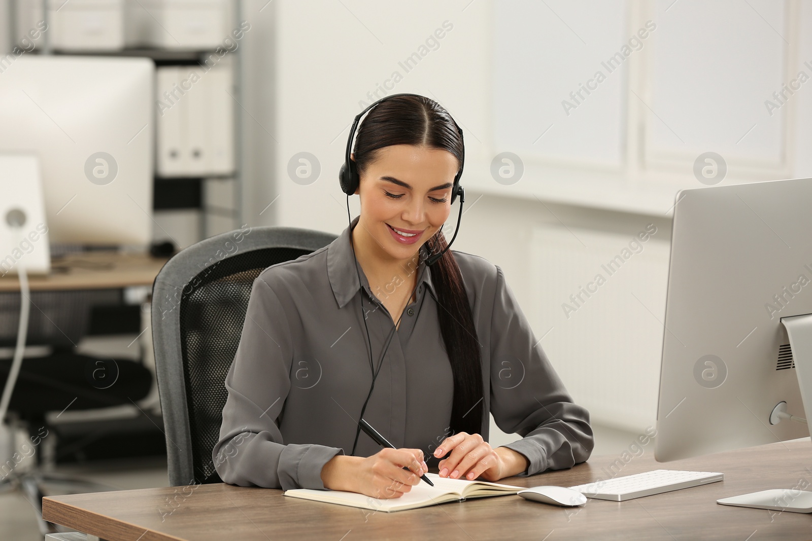 Photo of Hotline operator with headset and notebook working in office