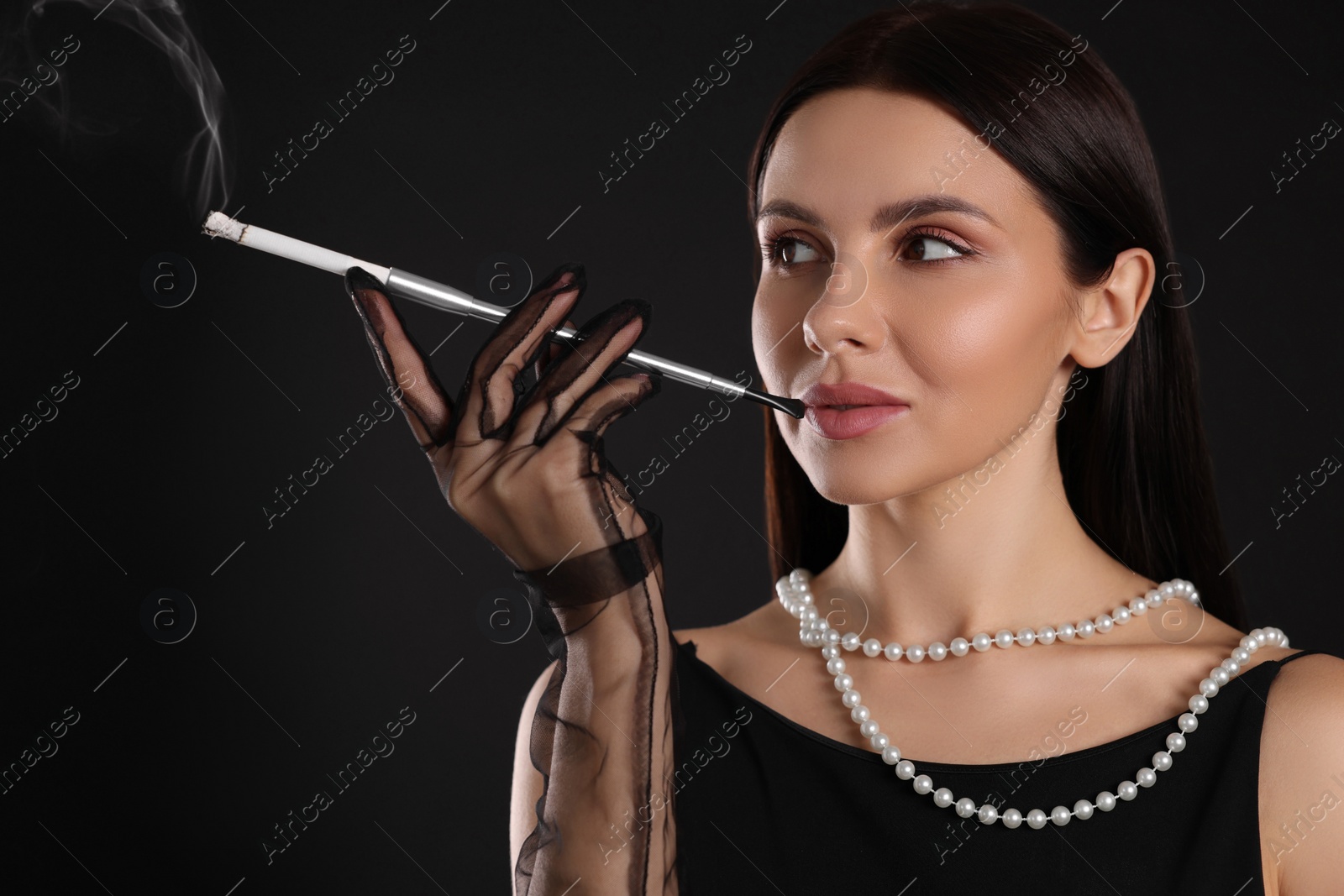 Photo of Woman using long cigarette holder for smoking on black background