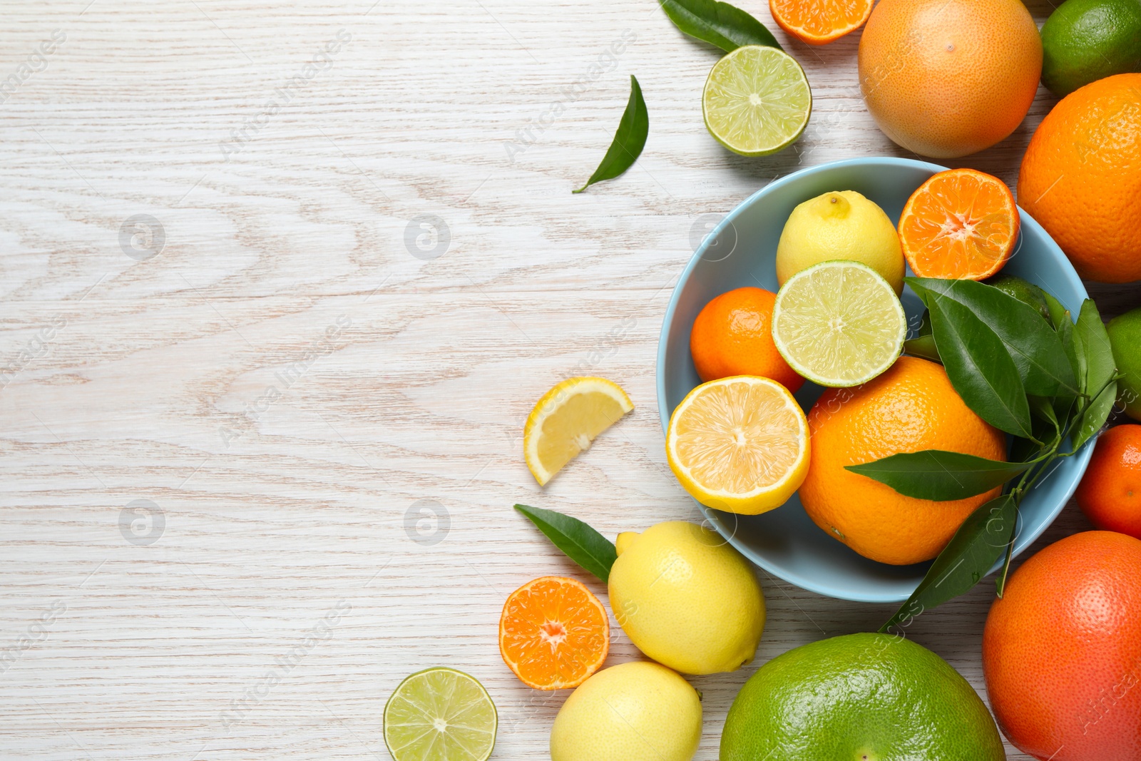 Photo of Different ripe citrus fruits with green leaves on white wooden table, flat lay. Space for text