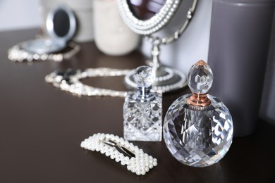 Luxury perfume bottles and stylish hair clip on wooden table, closeup