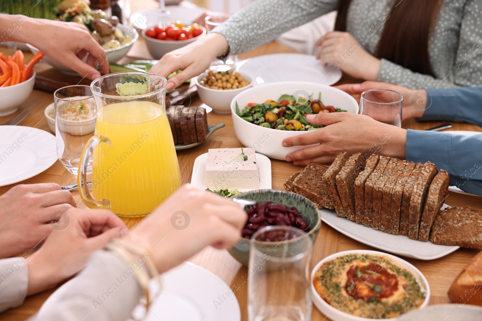 Photo of Friends eating vegetarian food at wooden table indoors, closeup