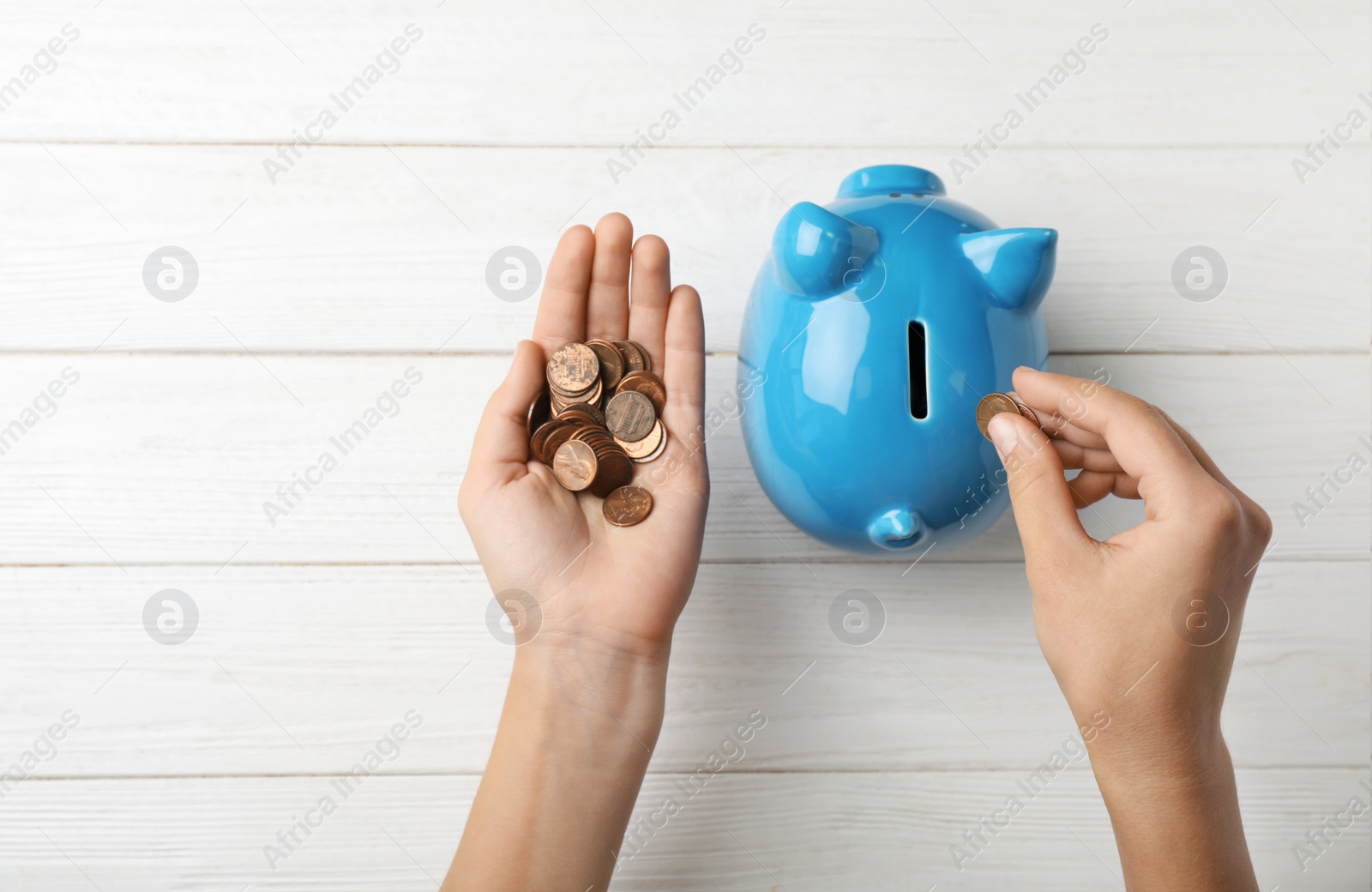 Photo of Woman putting coin into piggy bank on wooden table, top view