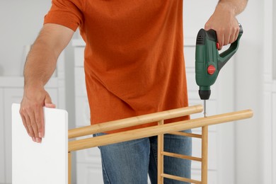 Photo of Man with electric screwdriver assembling shoe storage bench at home, closeup