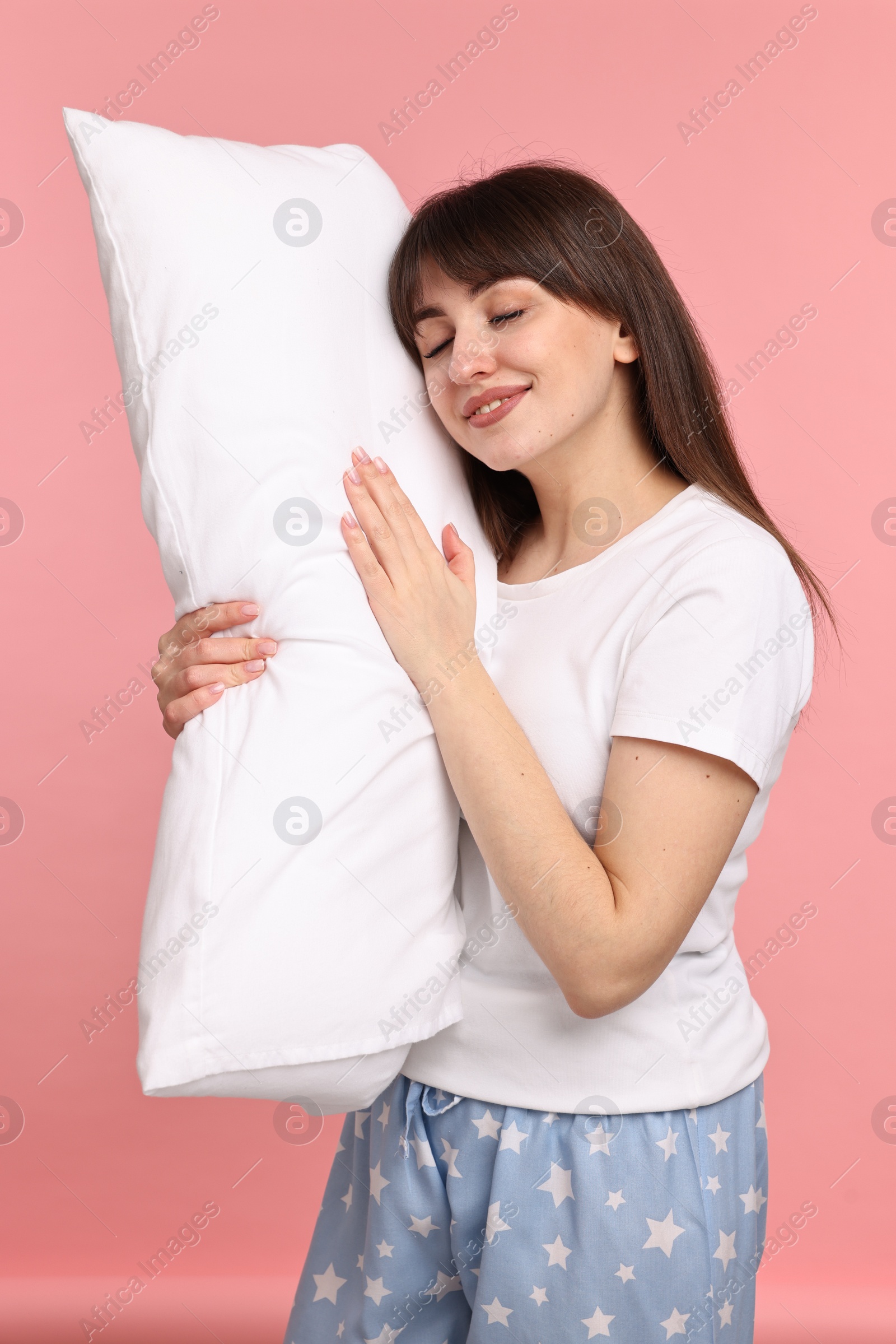 Photo of Happy woman in pyjama holding pillow on pink background