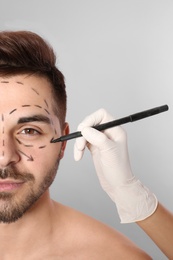 Doctor drawing marks on man's face for cosmetic surgery operation against grey background, closeup