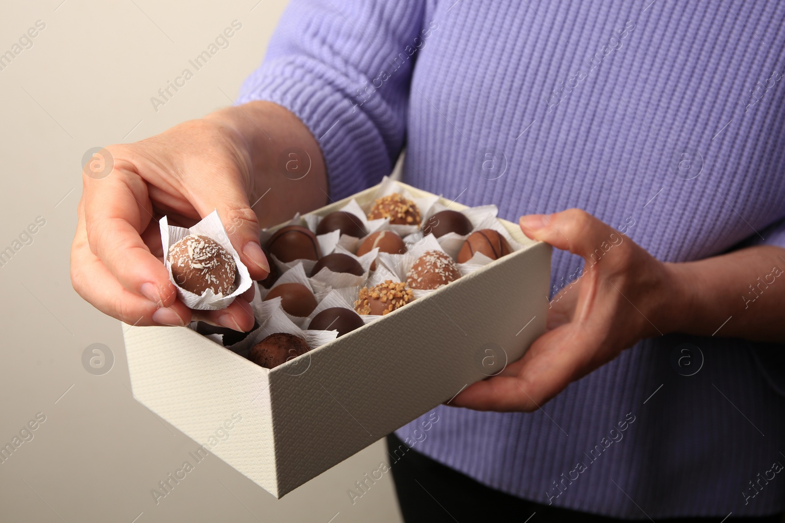 Photo of Woman taking delicious chocolate candy from box on light gray background, closeup