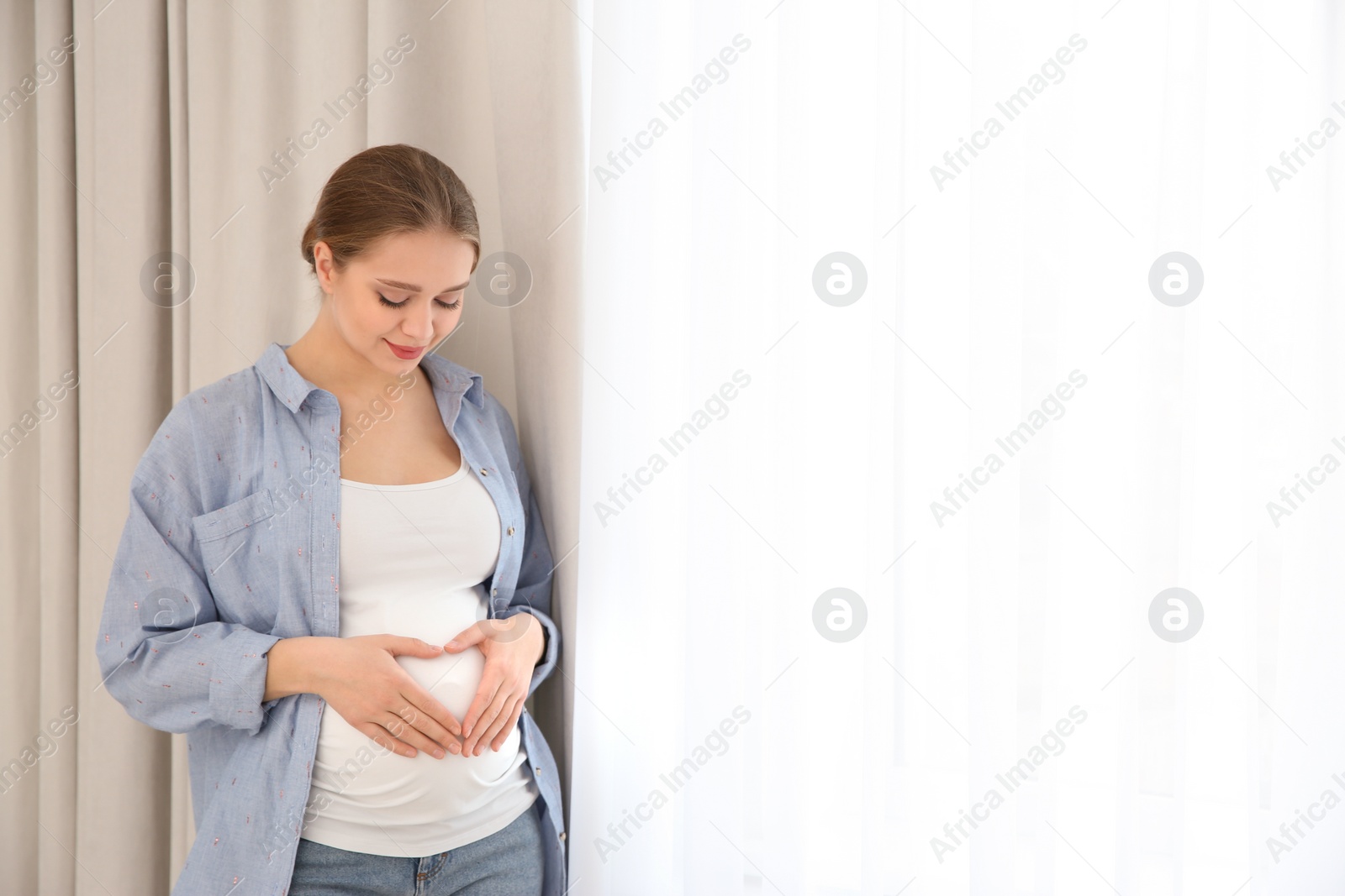 Photo of Young pregnant woman near window at home. Space for text