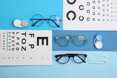 Vision test charts, glasses, lenses and tweezers on light blue background, flat lay
