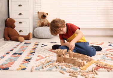 Photo of Little boy playing with wooden construction set on carpet in room, space for text. Child's toy