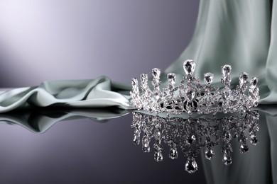 Photo of Beautiful silver tiara with gems near light cloth on dark mirror surface. Space for text