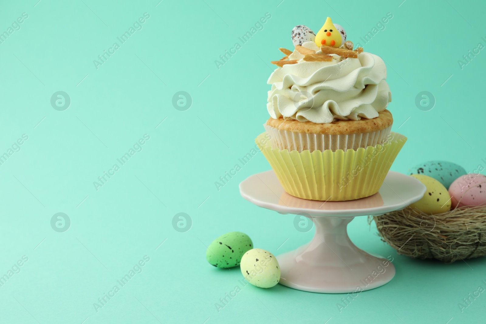 Photo of Tasty Easter cupcake with vanilla cream and festive decor on turquoise background, space for text