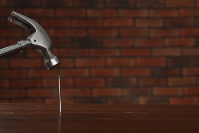 Photo of Hammering metal nail on wooden table against brick wall. Space for text