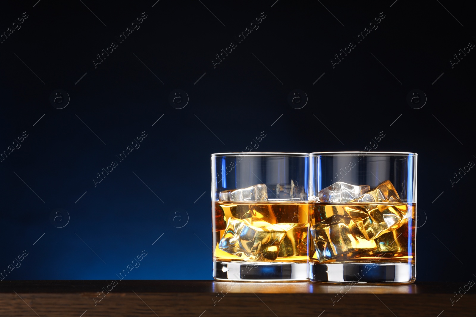 Photo of Whiskey with ice cubes in glasses on table against dark background. Space for text
